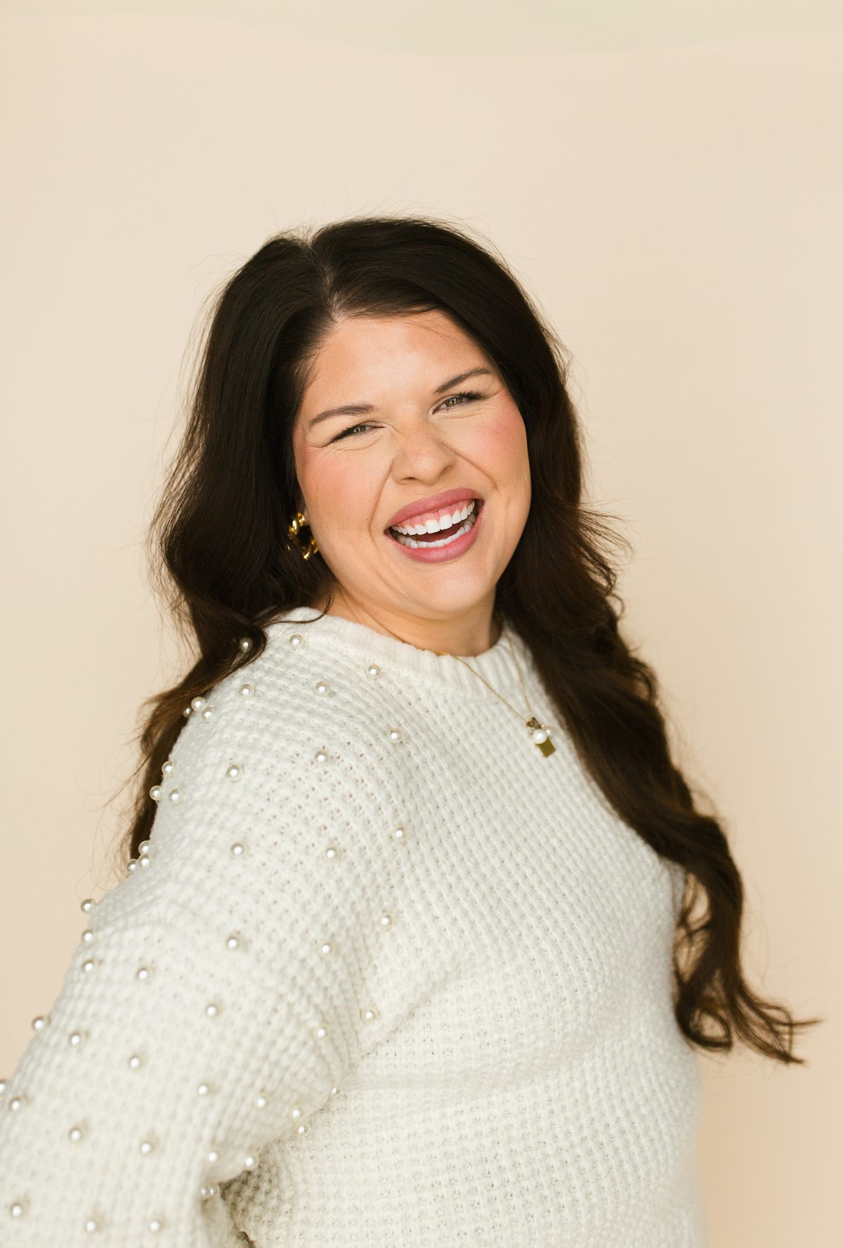 Liz Rodriguez laughing, wearing a cream pearl-studded sweater