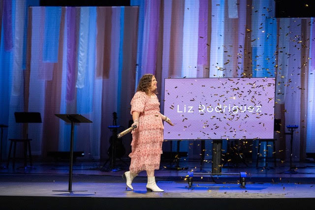 Liz walking onto a stage as confetti falls